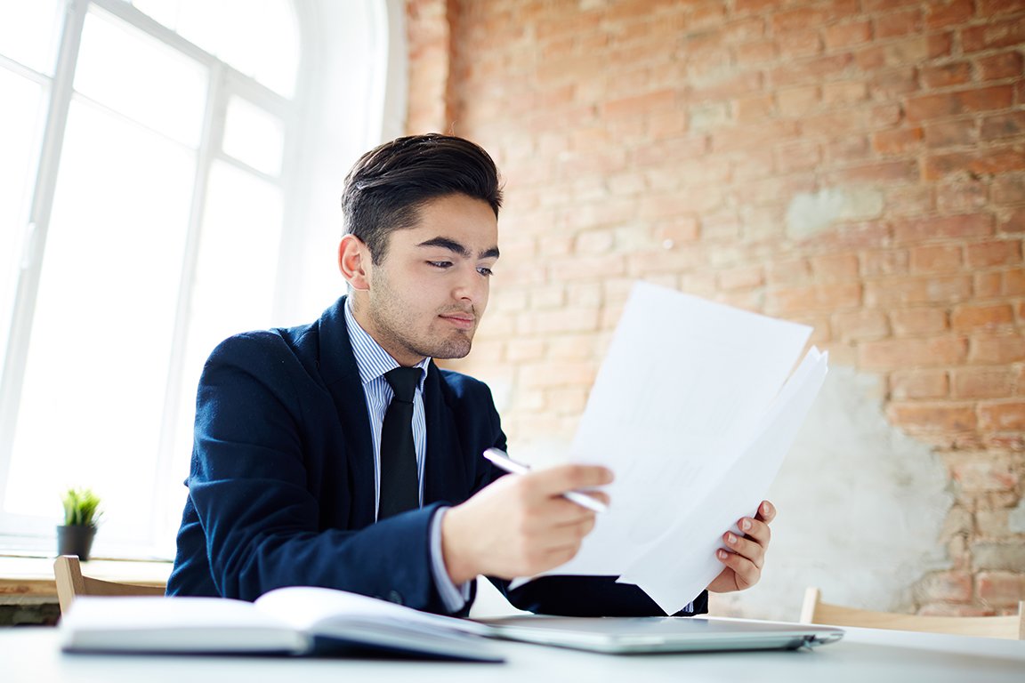 Young economist reading financial documents at workplace